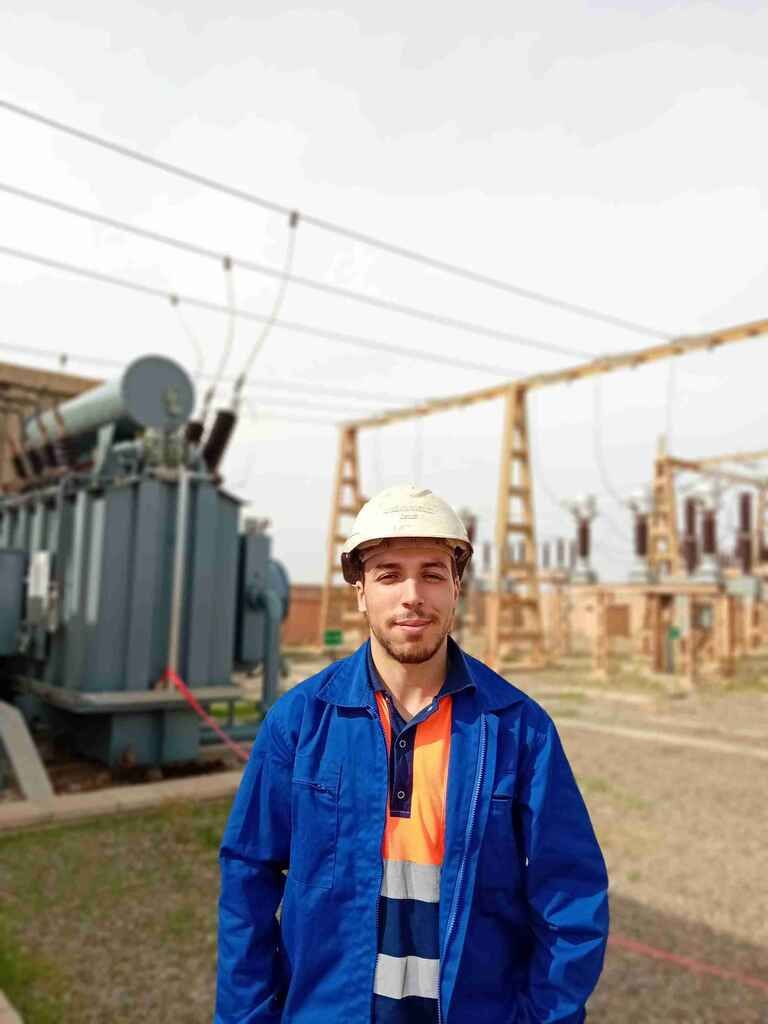 Mohsine Bakhcha en tenue de travail sur un site électrique industriel, devant un transformateur.
